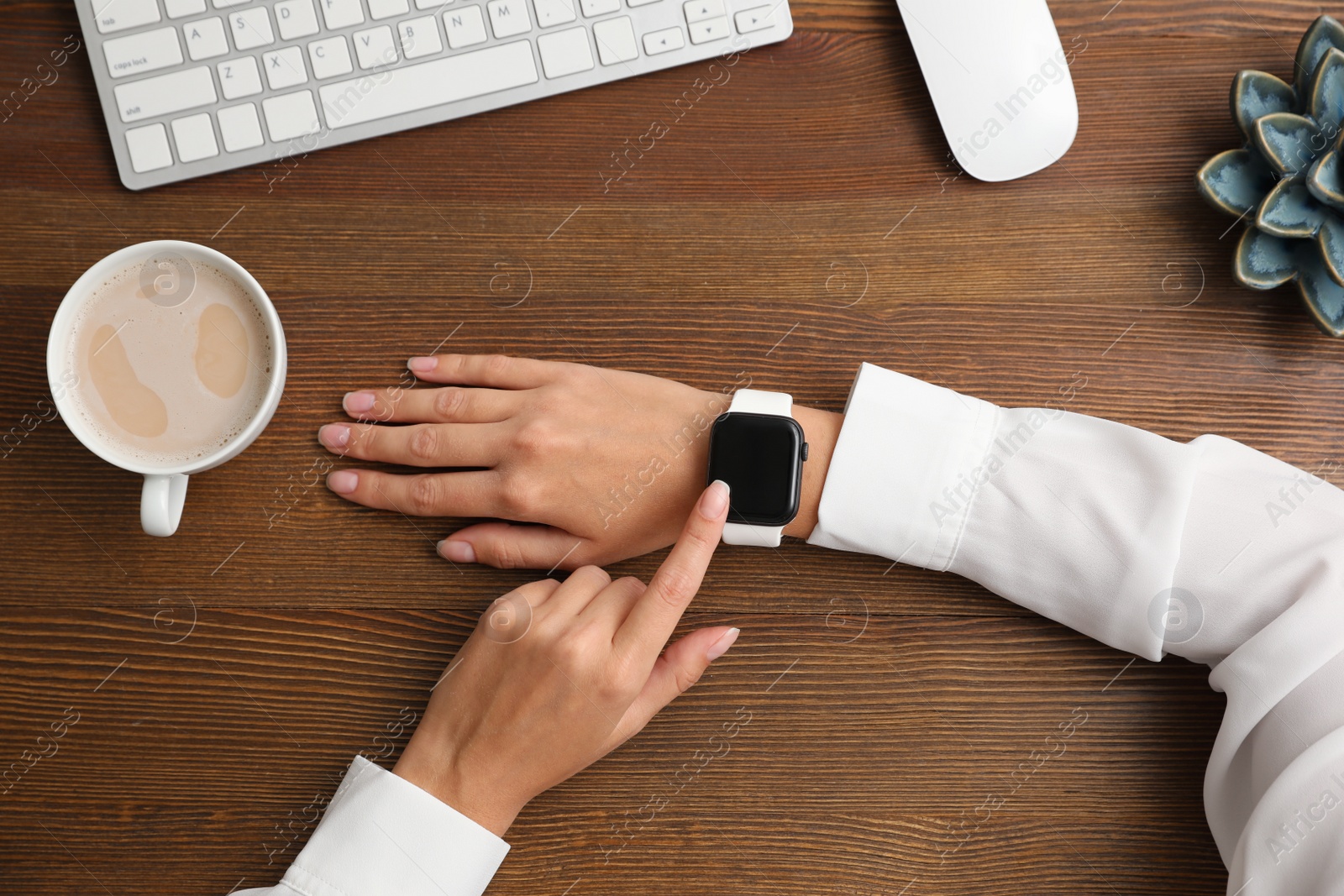 Image of Woman using stylish smart watch at wooden table, top view