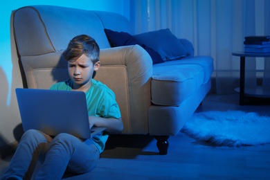 Photo of Upset little child with laptop in dark room. Danger of internet