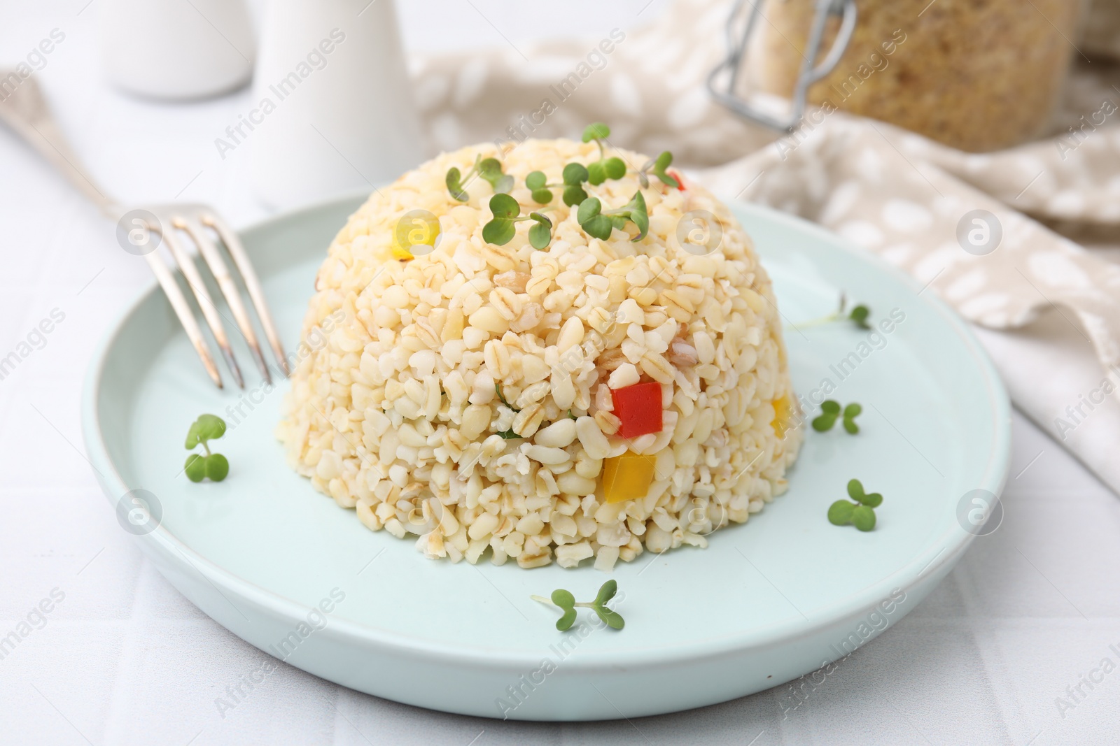 Photo of Delicious bulgur with vegetables and microgreens served on table, closeup