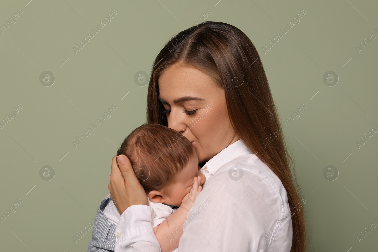 Photo of Mother kissing her cute newborn baby on olive background