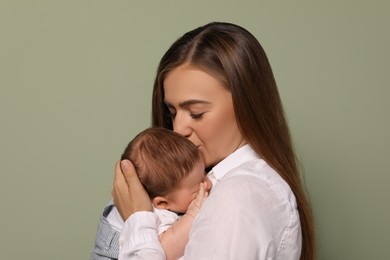 Mother kissing her cute newborn baby on olive background