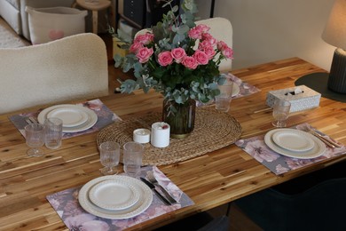 Beautiful table setting with bouquet of roses, napkins and candles in room