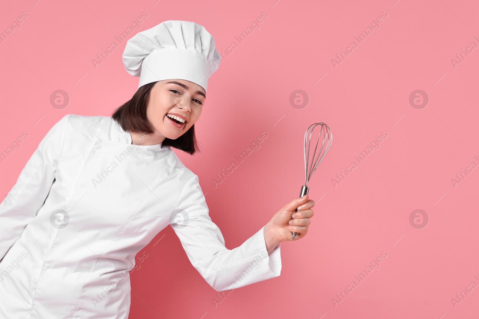 Photo of Happy confectioner with whisk on pink background, space for text