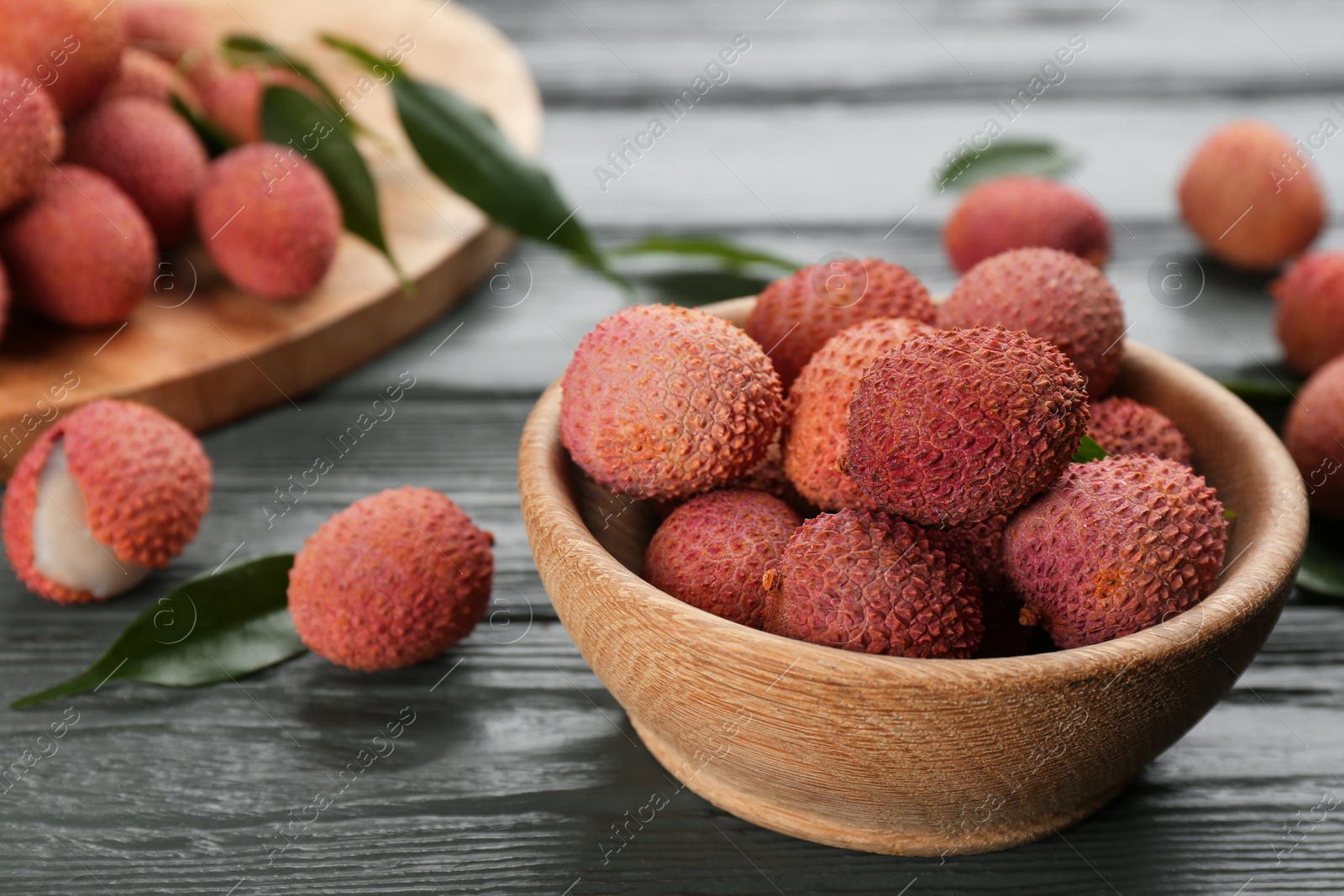 Photo of Fresh ripe lychee fruits in bowl on grey wooden table. Space for text