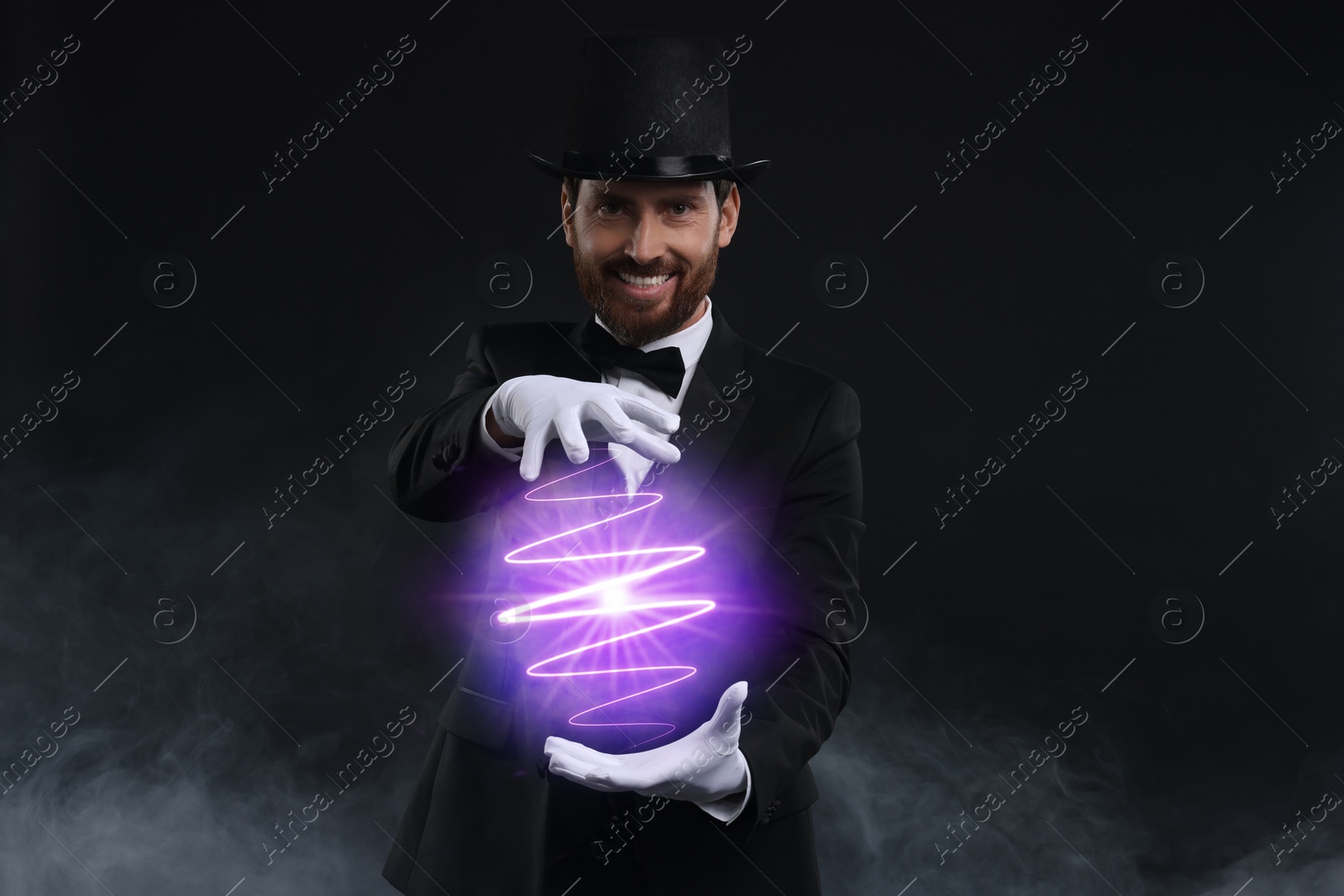 Image of Magic and sorcery. Magician with fantastic light in smoke on dark background