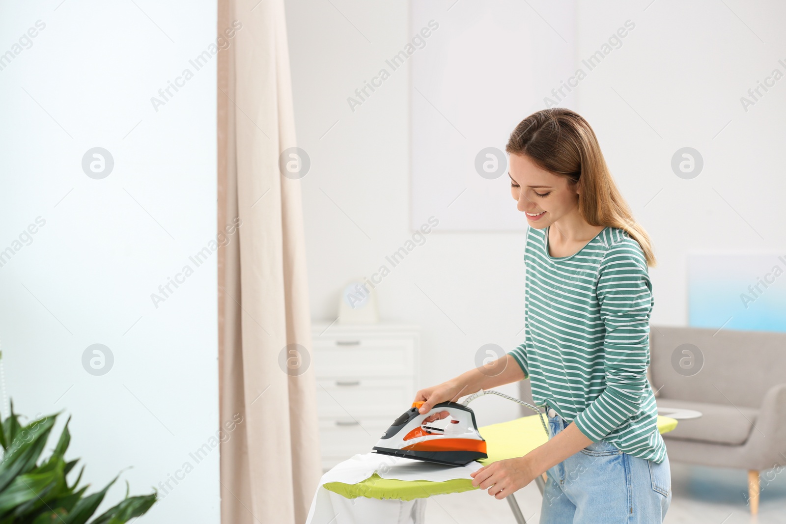 Photo of Young pretty woman ironing clean laundry indoors. Space for text