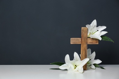 Photo of Composition with wooden cross and blossom lilies on table against color background, space for text