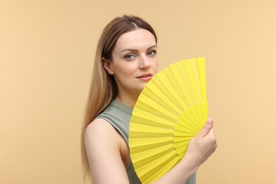 Beautiful woman with yellow hand fan on beige background