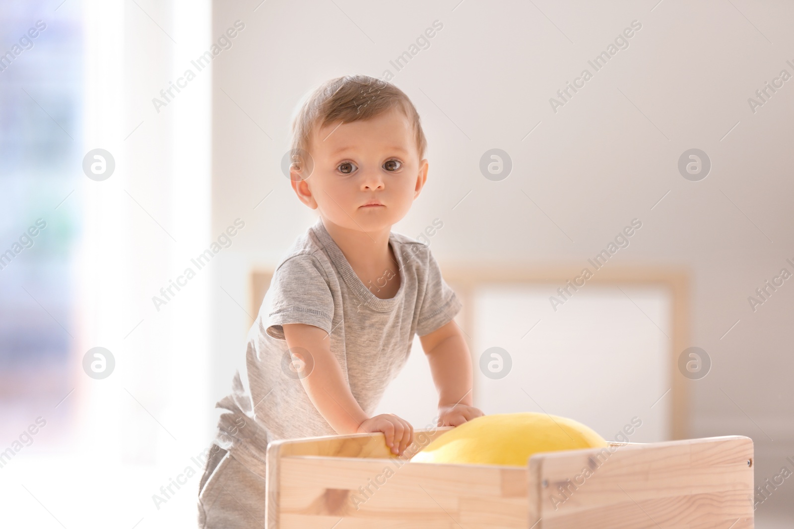 Photo of Cute baby holding on to wooden cart indoors. Learning to walk