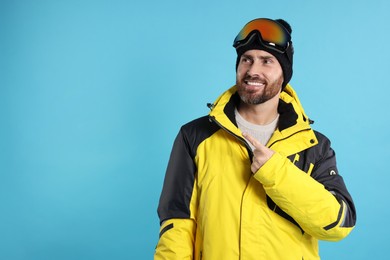 Photo of Winter sports. Happy man in ski suit and goggles on light blue background, space for text