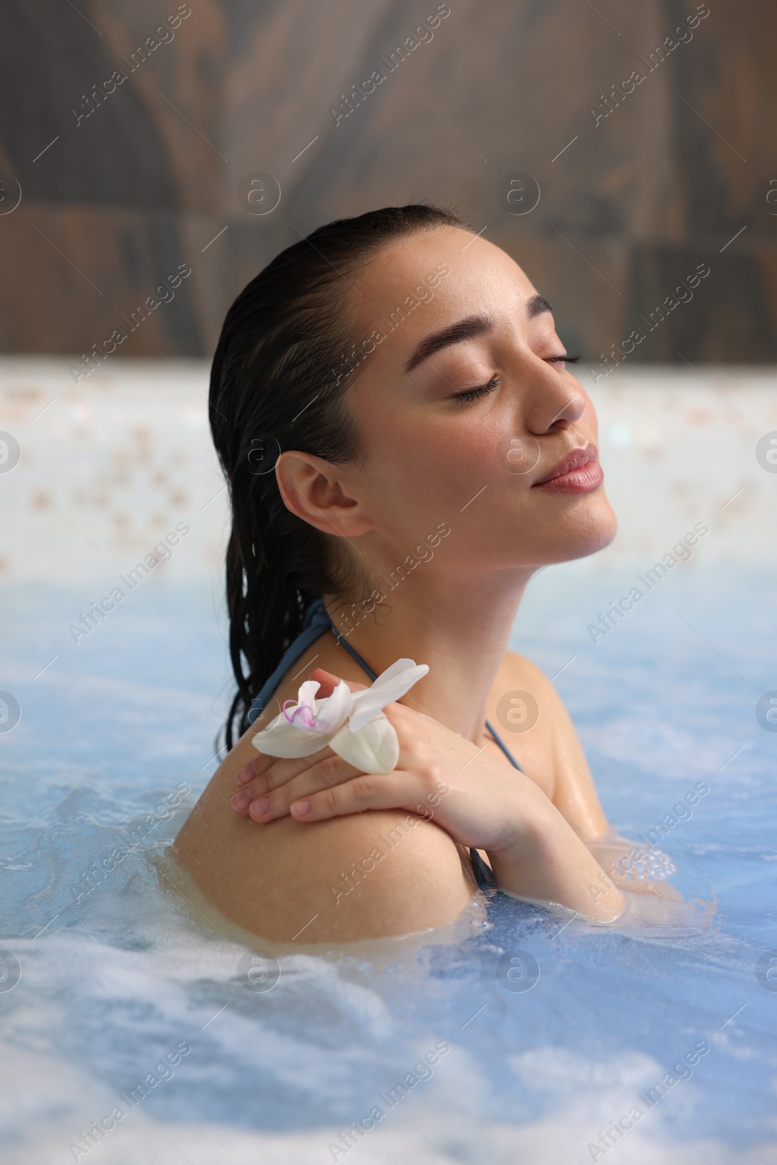 Photo of Beautiful woman with orchid flower relaxing in spa swimming pool