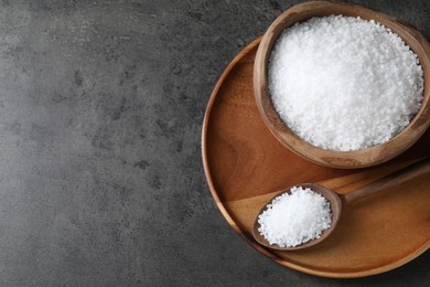 Photo of Natural salt in wooden bowl and spoon on dark grey table, top view. Space for text