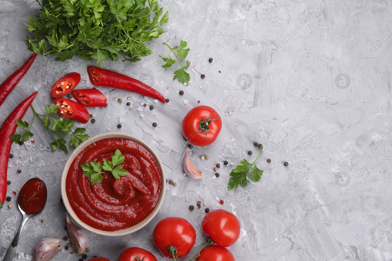 Photo of Flat lay composition with organic ketchup in bowl on grey textured table, space for text. Tomato sauce