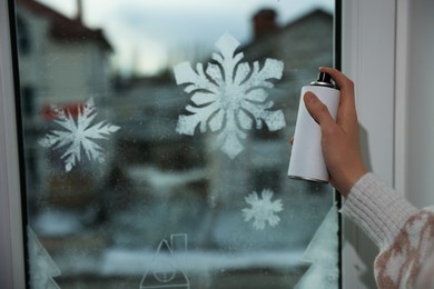 Woman using snow spray for decorating window with snowflakes at home, closeup