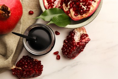 Photo of Glass jar of tasty pomegranate sauce and fresh ripe fruit on white marble table, flat lay