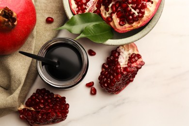 Glass jar of tasty pomegranate sauce and fresh ripe fruit on white marble table, flat lay