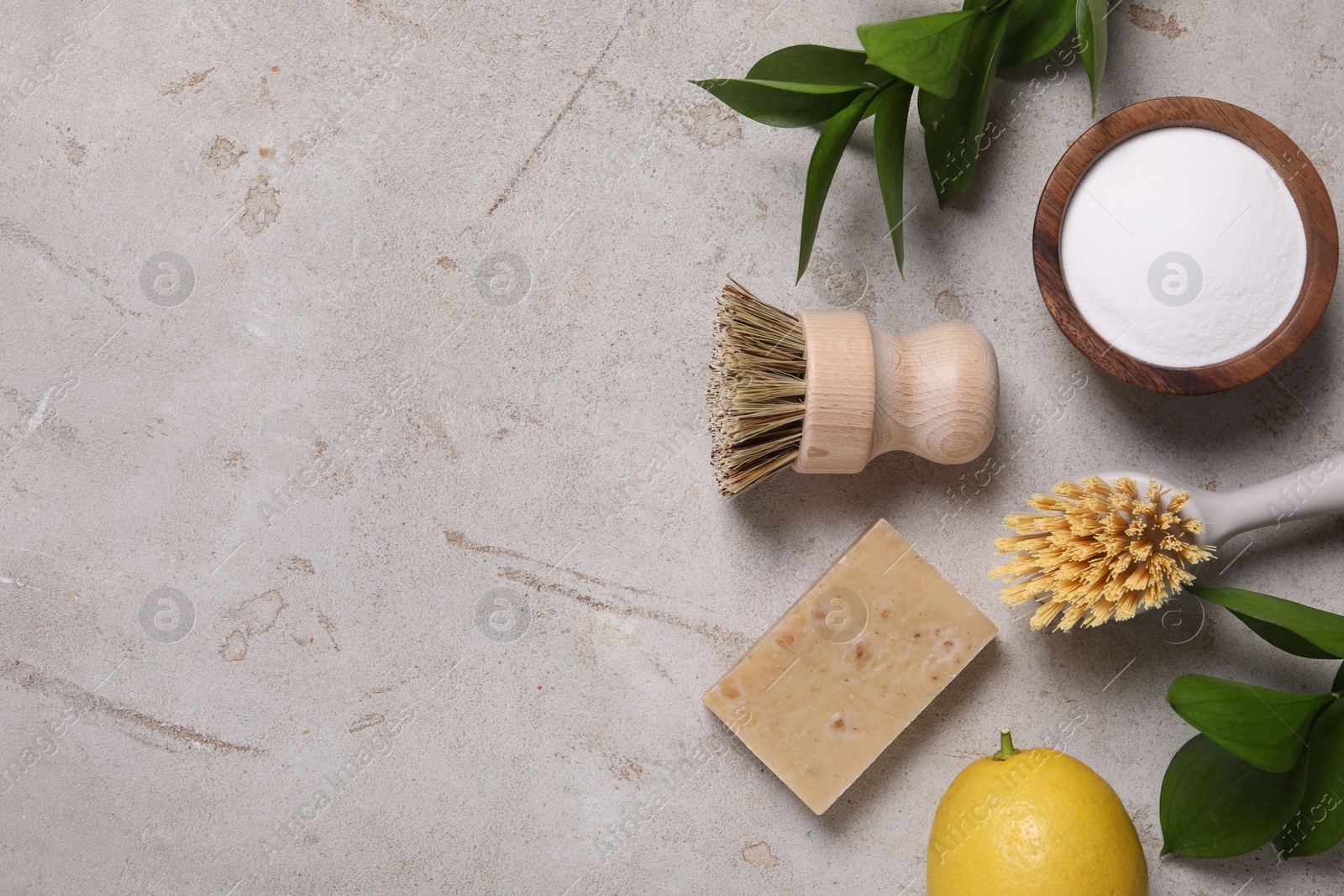 Photo of Cleaning brushes, baking soda, lemon, soap and green leaves on light grey table, flat lay. Space for text