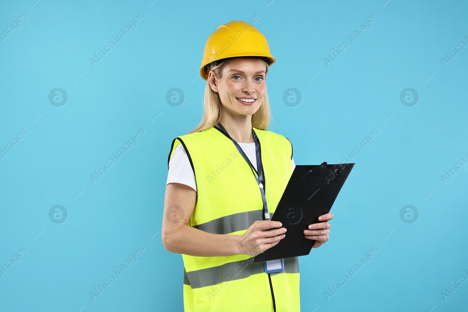 Photo of Engineer in hard hat holding clipboard on light blue background