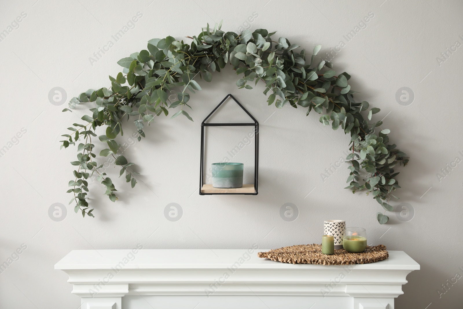 Photo of Beautiful garland made of eucalyptus branches and aromatic candle hanging above mantelpiece indoors