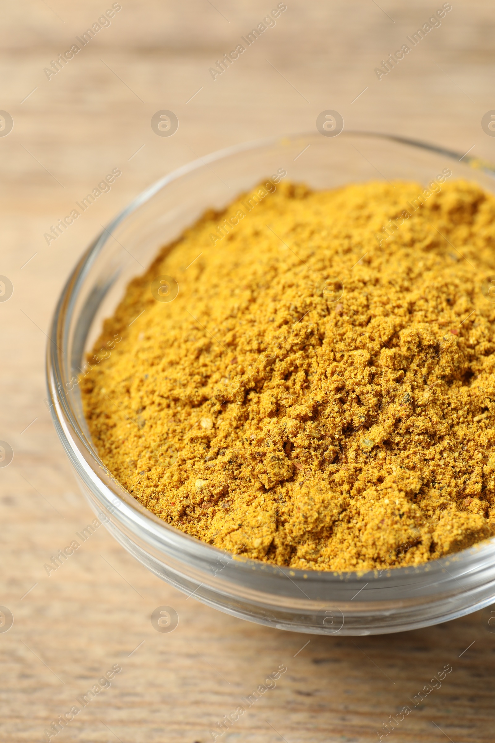 Photo of Curry powder in bowl on wooden table, closeup