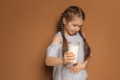 Photo of Little girl with dairy allergy holding glass of milk on color background