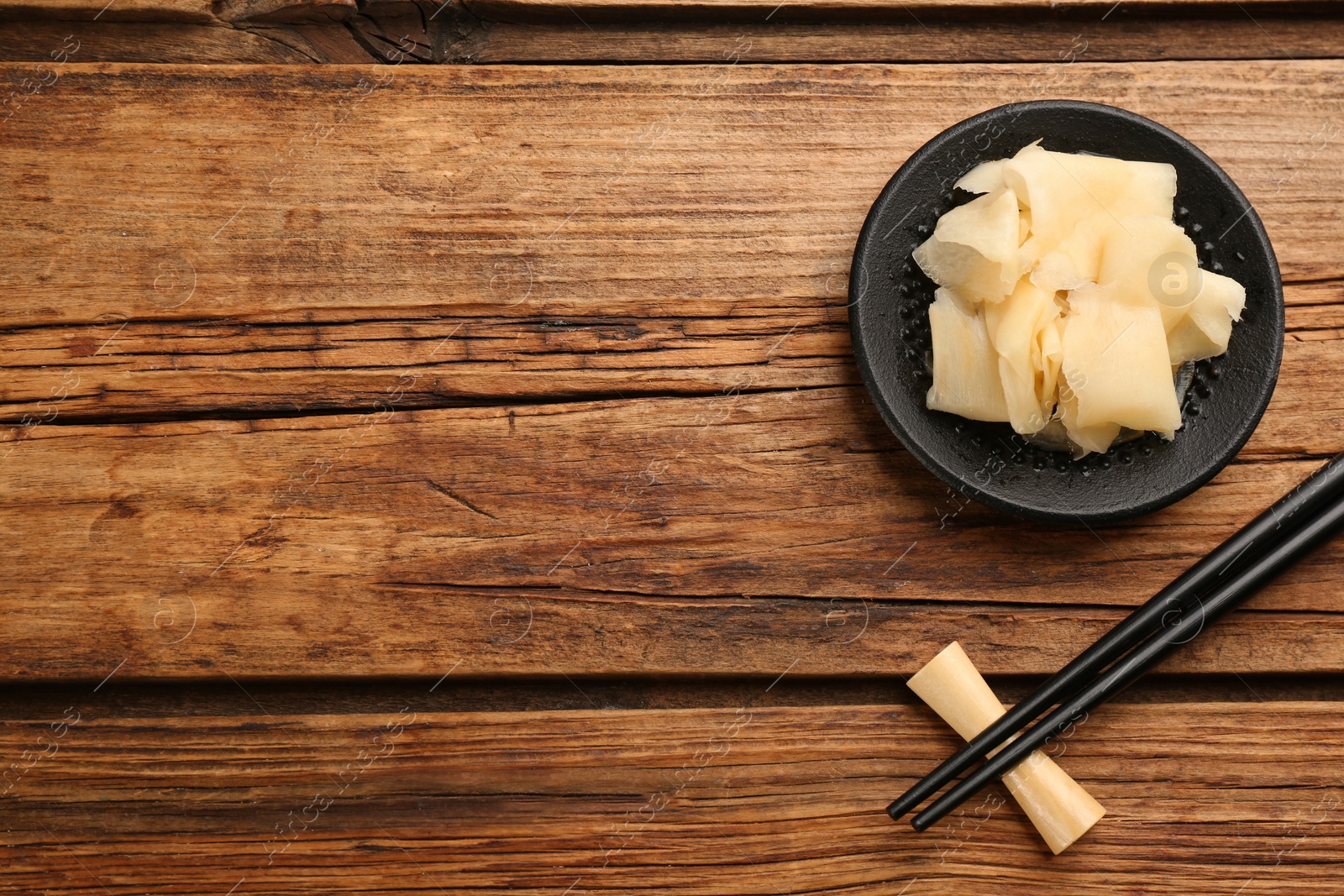 Photo of Spicy pickled ginger and chopsticks on wooden table, flat lay. Space for text