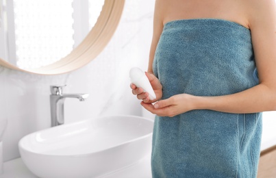 Photo of Young woman with roll on deodorant in bathroom, closeup view. Space for text