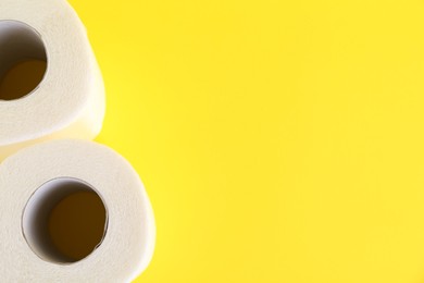 Photo of Soft toilet paper rolls on yellow background, top view. Space for text