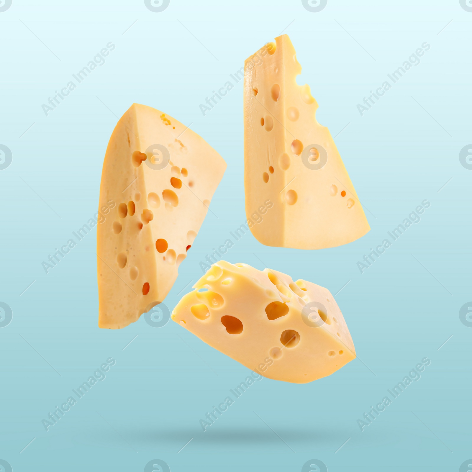 Image of Pieces of tasty cheese falling on light blue background