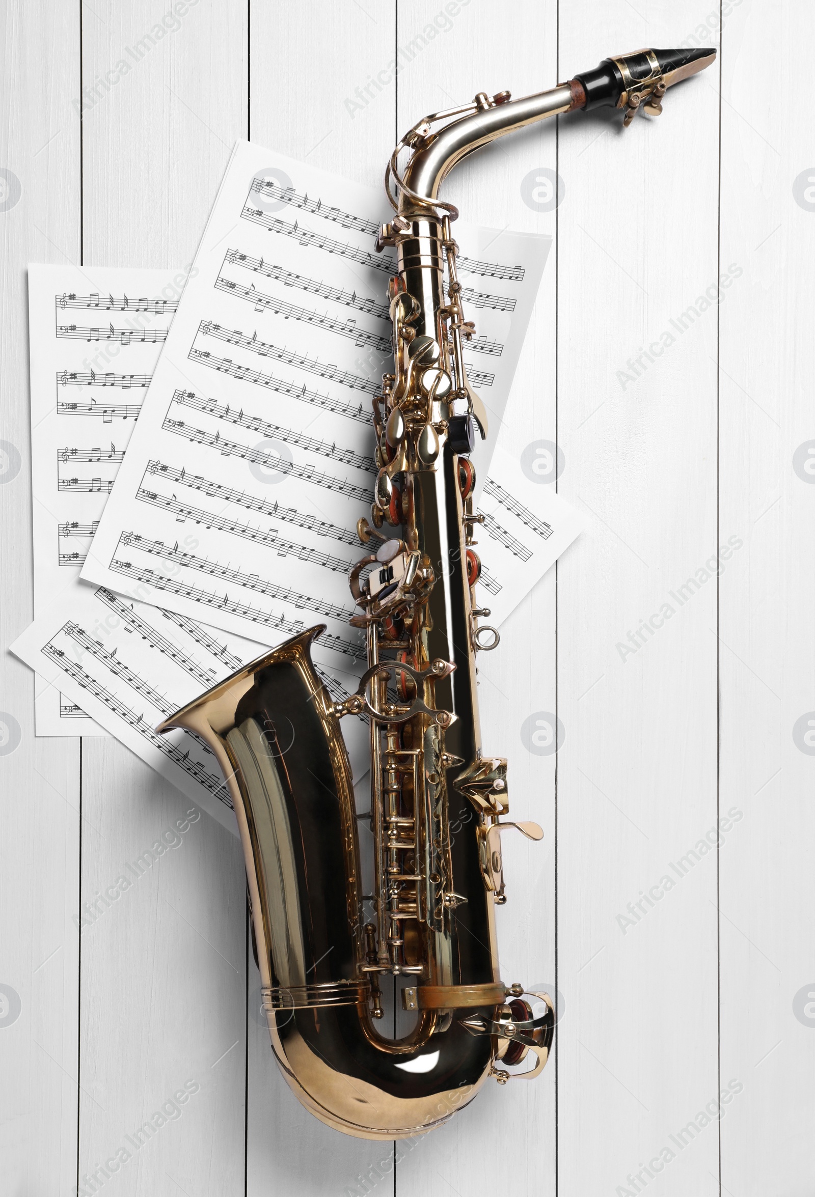 Photo of Beautiful saxophone and note sheets on white wooden background, flat lay