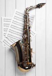 Photo of Beautiful saxophone and note sheets on white wooden background, flat lay