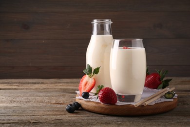 Photo of Tasty yogurt in glass, bottle, straws and berries on wooden table. Space for text