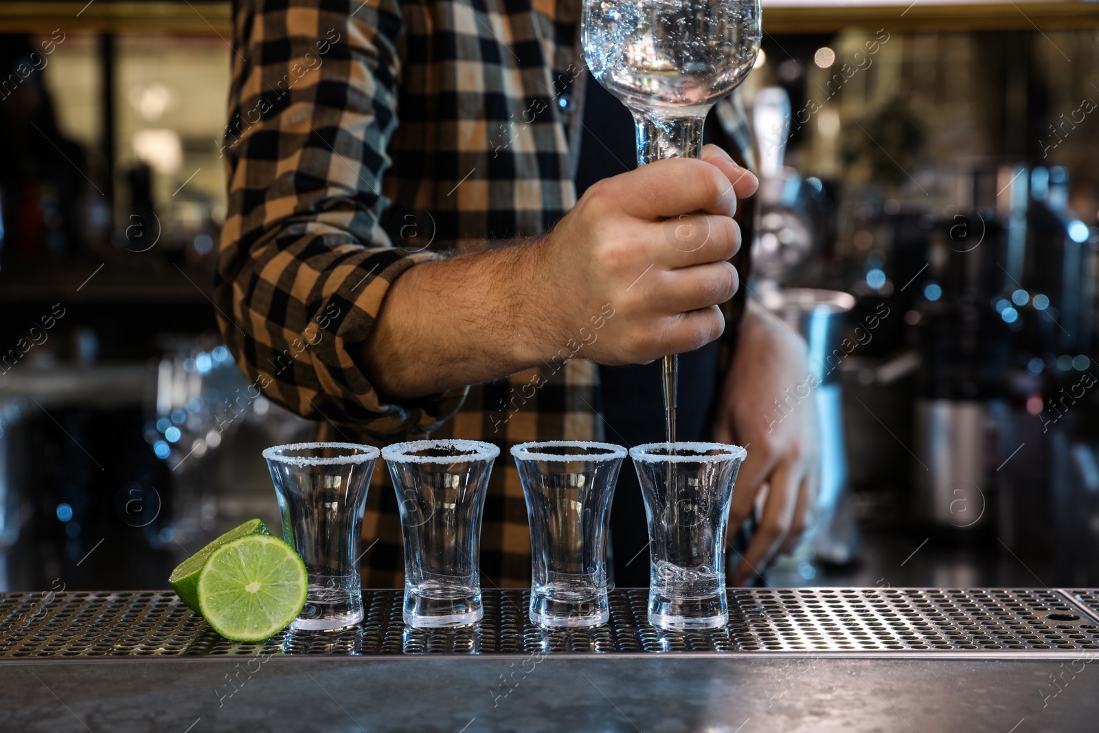 Photo of Bartender pouring Mexican Tequila into shot glasses at bar counter, closeup