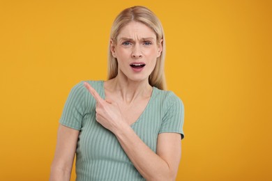 Surprised woman pointing at something on yellow background