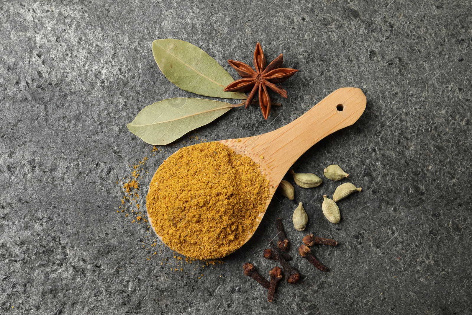 Photo of Spoon with dry curry powder and other spices on dark textured table, flat lay