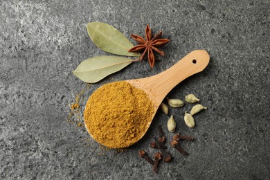 Spoon with dry curry powder and other spices on dark textured table, flat lay