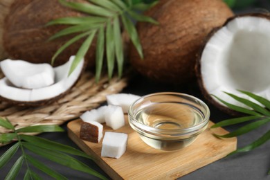 Photo of Organic coconut cooking oil, leaves and fresh fruits on grey table, closeup