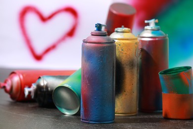 Photo of Many spray paint cans on gray surface against color background