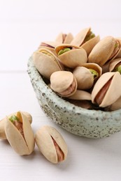 Photo of Delicious pistachios in bowl on white table, closeup