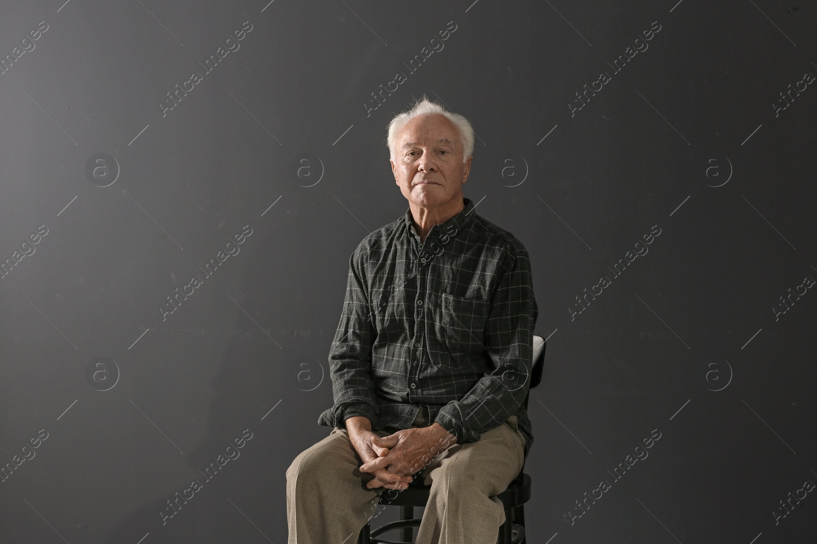 Photo of Portrait of poor elderly man sitting on chair against dark background