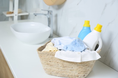 Photo of Bottles of detergent and children's clothes on countertop in bathroom. Space for text