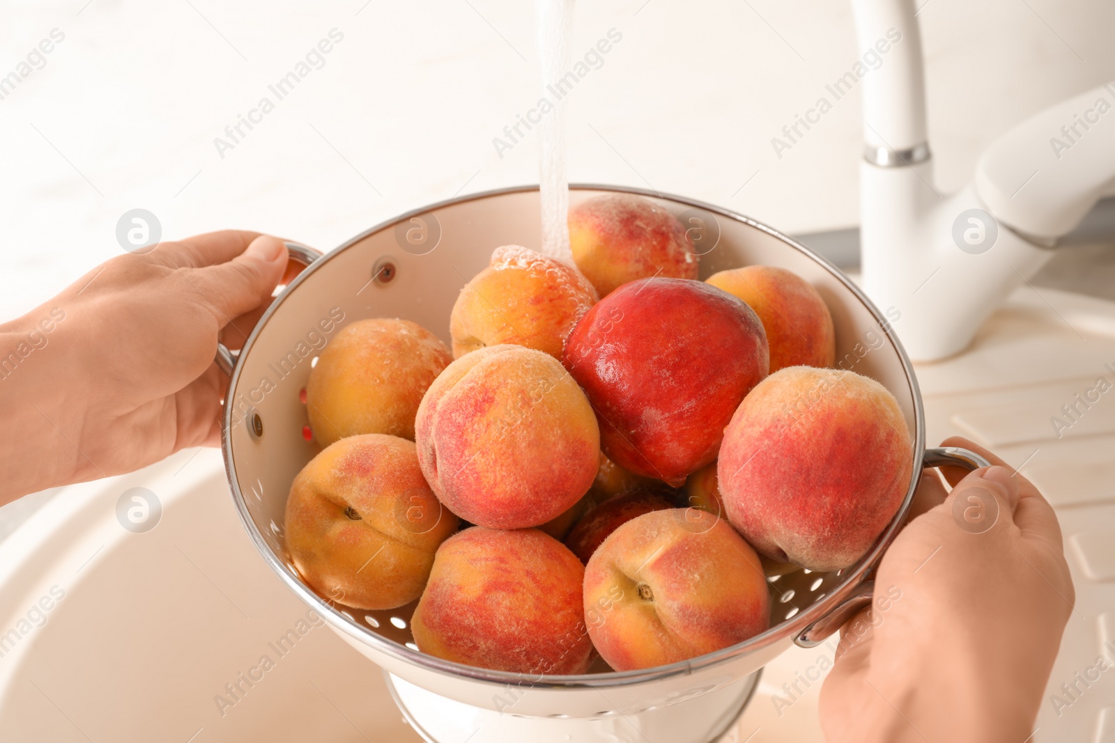 Photo of Woman washing fresh sweet peaches in kitchen