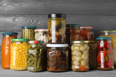 Jars with pickled vegetables on wooden table against grey background