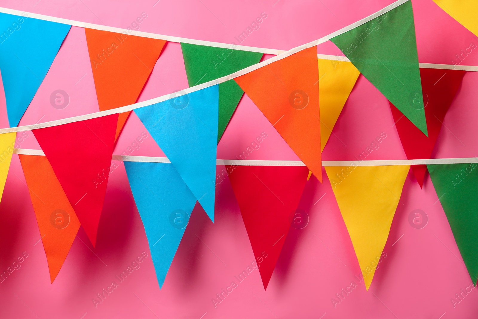 Photo of Buntings with colorful triangular flags hanging on pink background. Festive decor