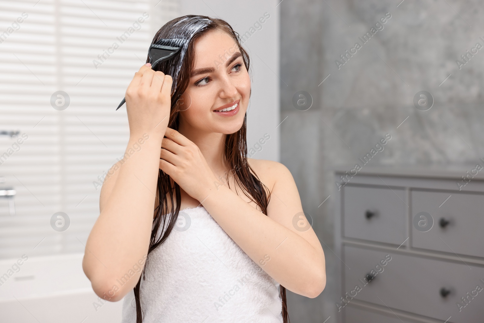Photo of Young woman applying hair mask in bathroom. Space for text