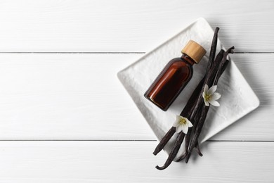 Photo of Vanilla pods, essential oil and flowers on white wooden table, top view. Space for text