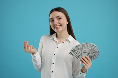 Photo of Happy woman with dollar banknotes showing money gesture on light blue background