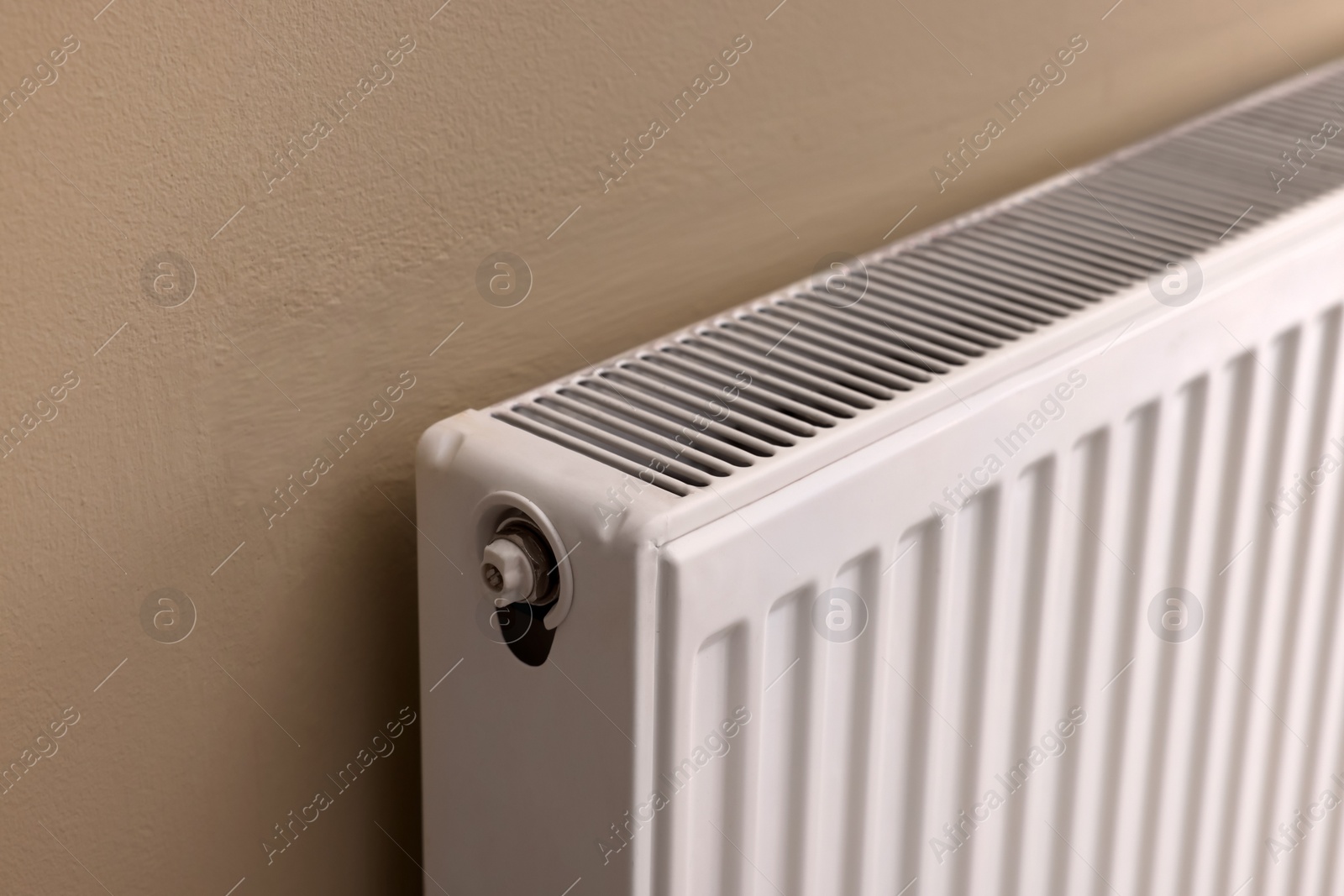 Photo of Modern radiator on beige wall, closeup. Central heating system