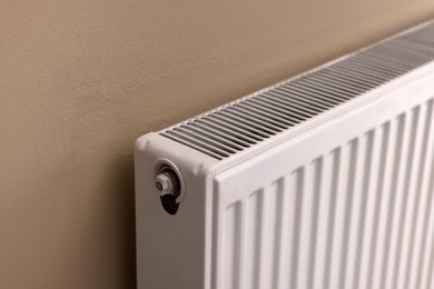 Photo of Modern radiator on beige wall, closeup. Central heating system