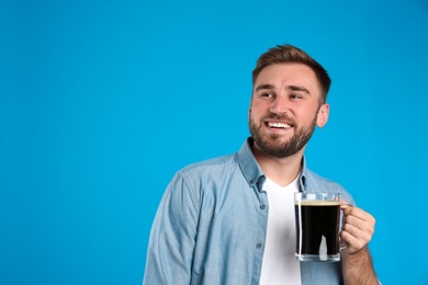 Photo of Handsome man with cold kvass on blue background. Traditional Russian summer drink